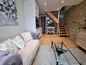 Ein Wohnzimmer mit einer Couch, einem Couchtisch, einer Treppe, einer Küchenzeile und einer Steinwand.