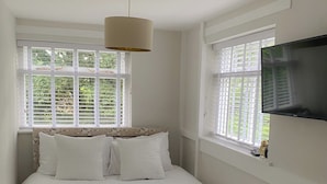 A neatly made bed with white bedding and two folded towels, a ceiling lamp, and a TV mounted on the wall.