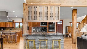 A spacious kitchen with wooden cabinets, a central island with stools, and a stone countertop.