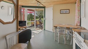 A cozy room with a wooden ceiling, a dining table with chairs, a TV, and a kitchen area with a stove.