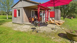 A rustic wooden cabin with a covered patio, outdoor seating, and a barbecue grill.