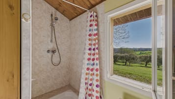 Une douche avec un plafond en bois, une fenêtre donnant sur un paysage verdoyant et un rideau de douche à pois.