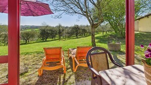 A covered patio with two orange chairs and a table, overlooking a vineyard. - Chalet La Brousse No. 2 – sleeps 5 – with pool (Salignac-Eyvigues)