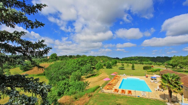 A large swimming pool surrounded by lounge chairs and umbrellas, set in a lush green landscape with hills in the background. - Chalet La Brousse No. 2 – sleeps 5 – with pool (Salignac-Eyvigues)