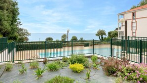 A pool area with a view of the sea, surrounded by a green fence and various plants. - Apart 100m from the beach - swimming pool for 4 (Pornic)