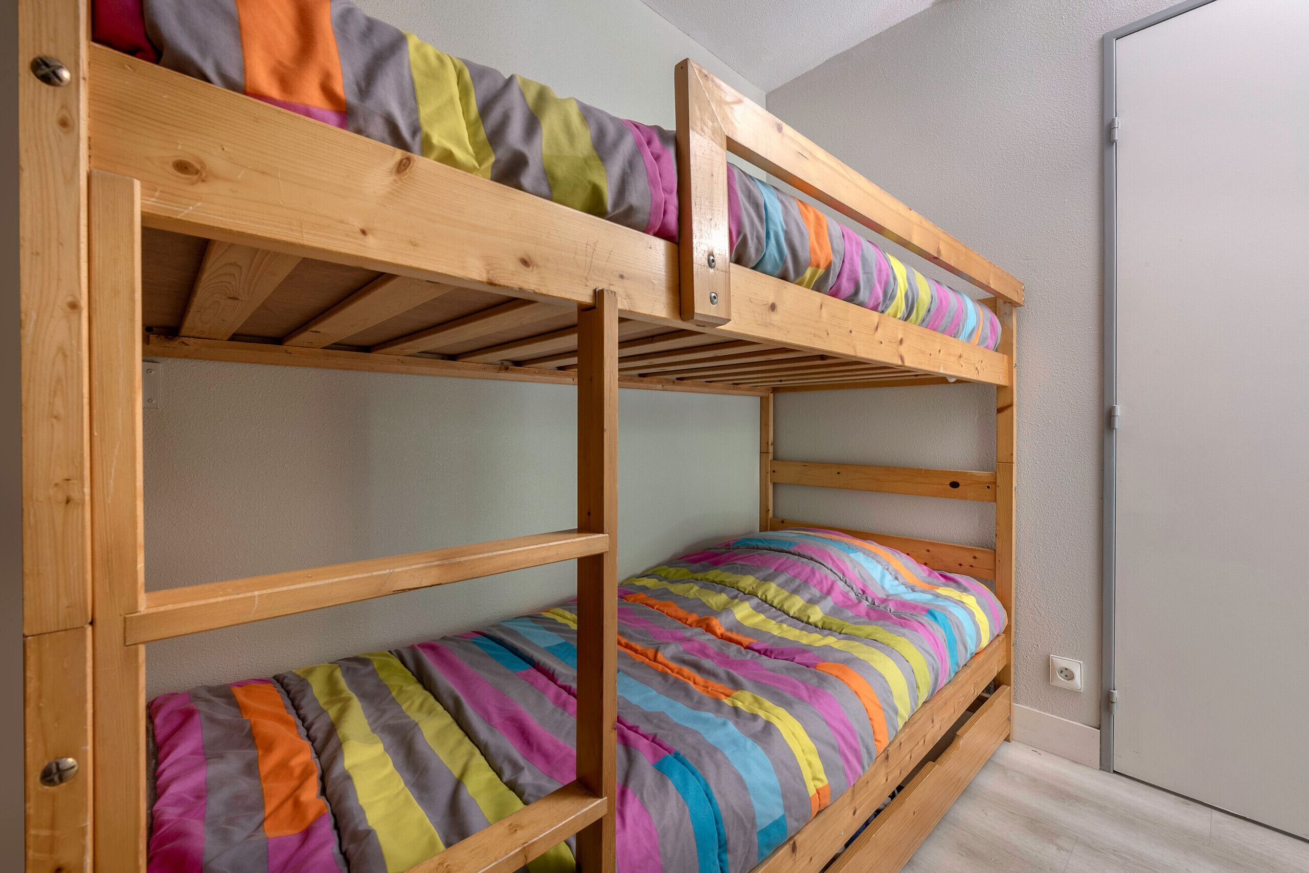 Uma cama beliche com roupa de cama colorida em um quarto com porta e paredes claras.