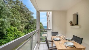 A balcony with a dining table set for four, overlooking a lush green landscape and the sea. - Apart 100m from the beach - swimming pool for 4 (Pornic)