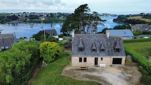 A stone house with a sloped roof, a small porch, and a view of a harbor with boats. - View over the Aber - House for 8 - Large garden (Lannilis)