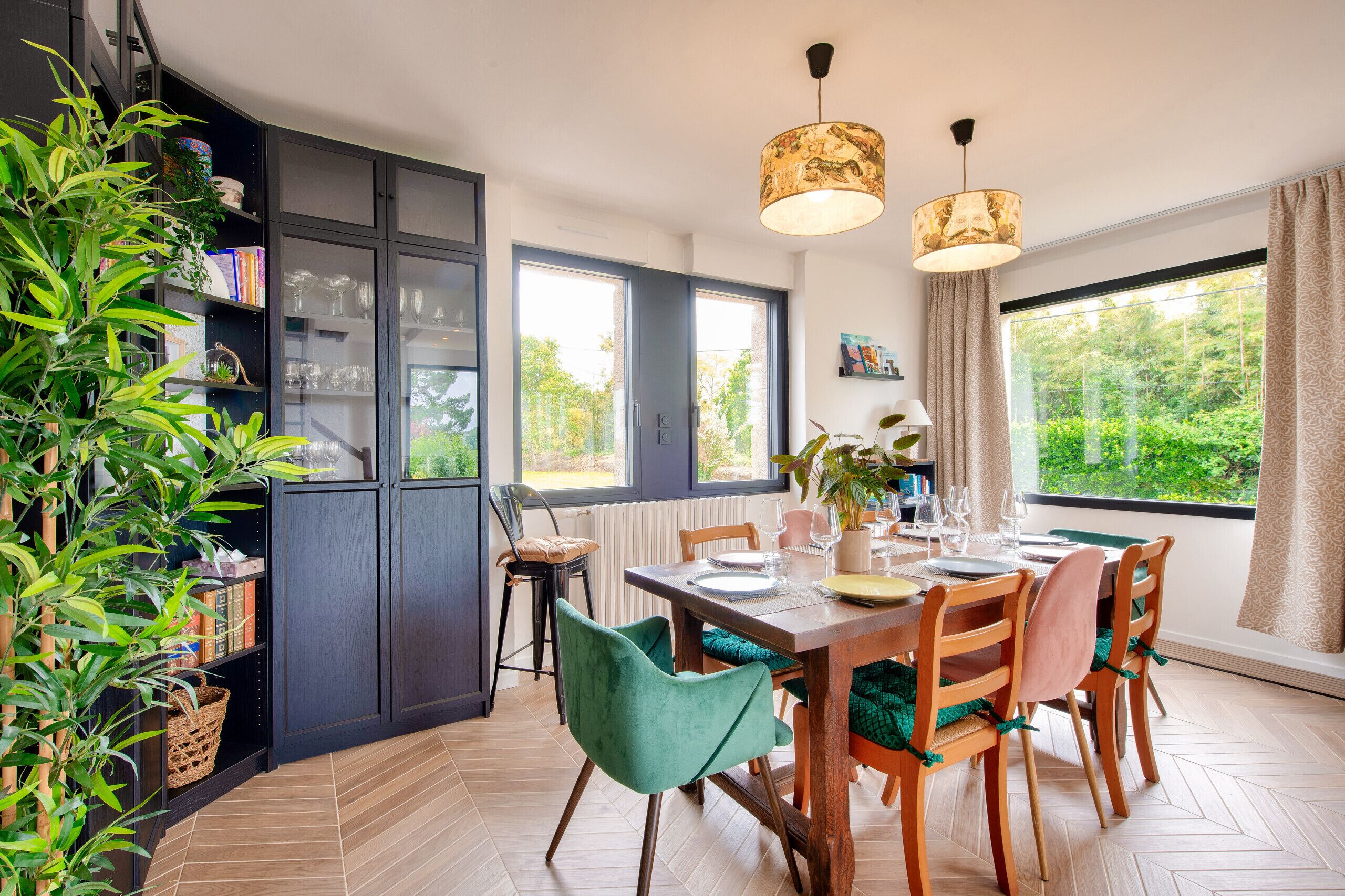 A modern kitchen with a dining area, featuring a large window, wooden cabinets, and a variety of chairs.