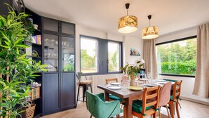 A modern kitchen with a dining area, featuring a large window, wooden cabinets, and a variety of chairs. - View over the Aber - House for 8 - Large garden (Lannilis)