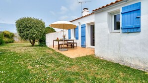 A white building with blue shutters, a patio with a table and chairs, and a tree.