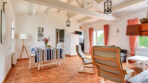 A spacious room with a tiled floor, a dining area with a striped tablecloth, a wooden chair, and a white sofa.