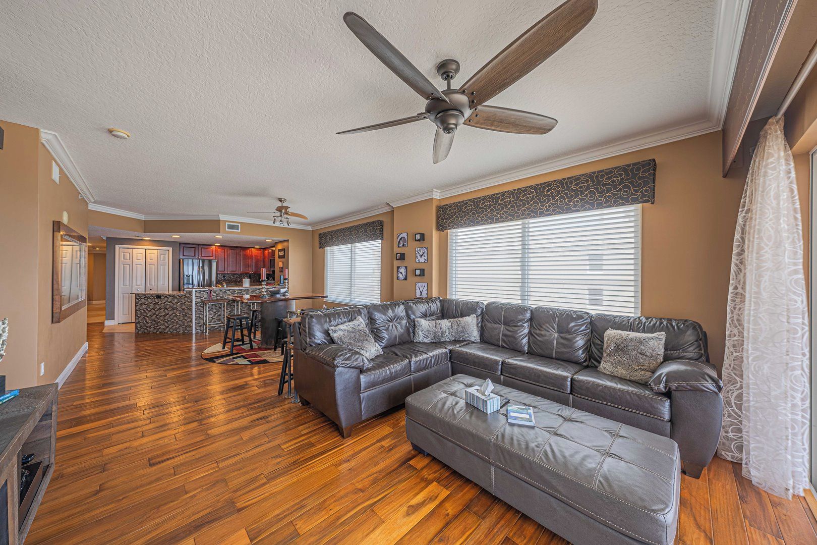 A spacious living room with a large sectional sofa, a ceiling fan, and hardwood flooring.
