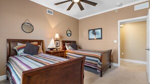 A bedroom with two wooden beds, a ceiling fan, and a nightstand with a lamp.