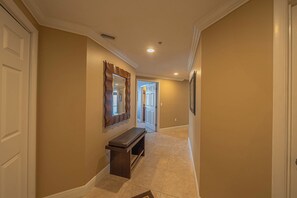 A hallway with beige walls, a wooden bench, and a mirror.