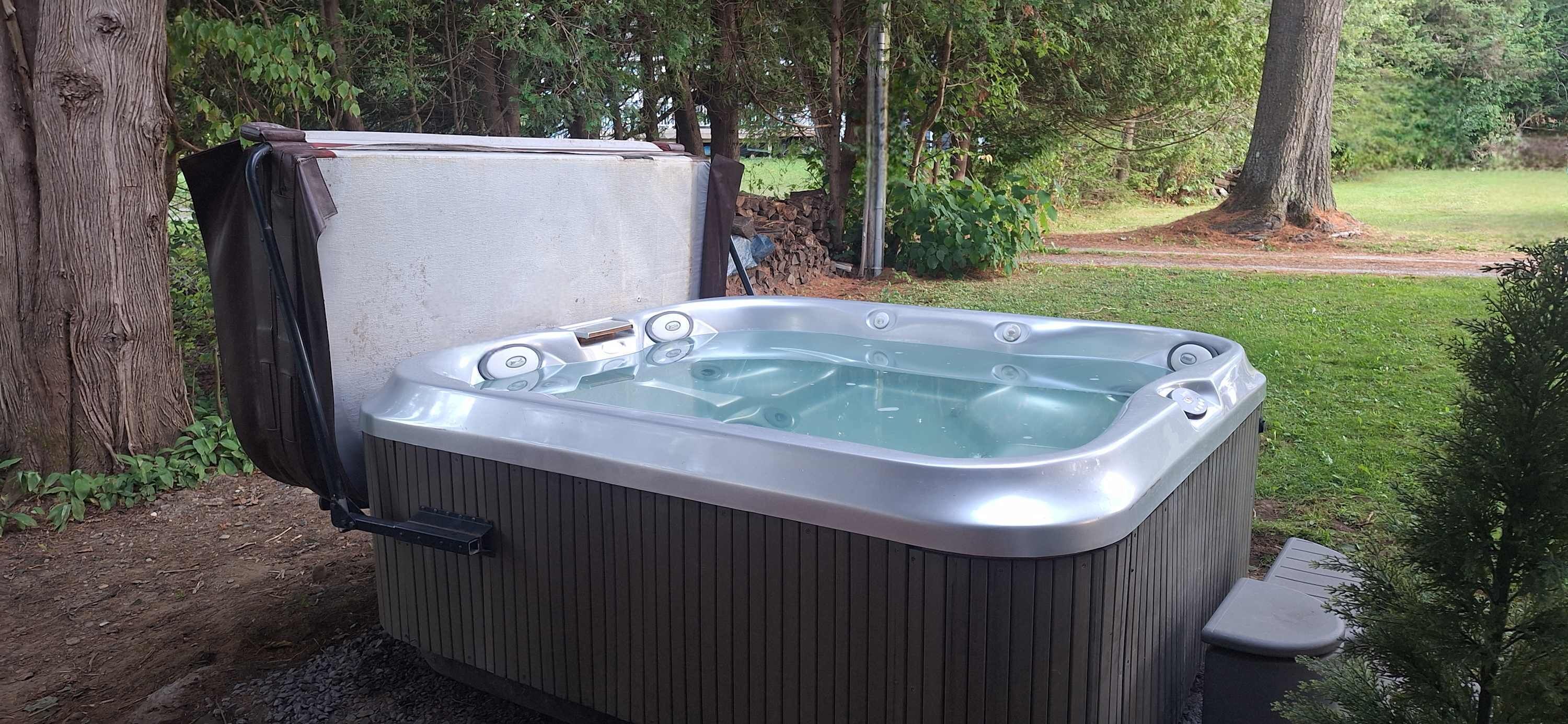 Un bain à remous installé dans un jardin, avec une structure en bois, entouré d’arbres et d’une pelouse.