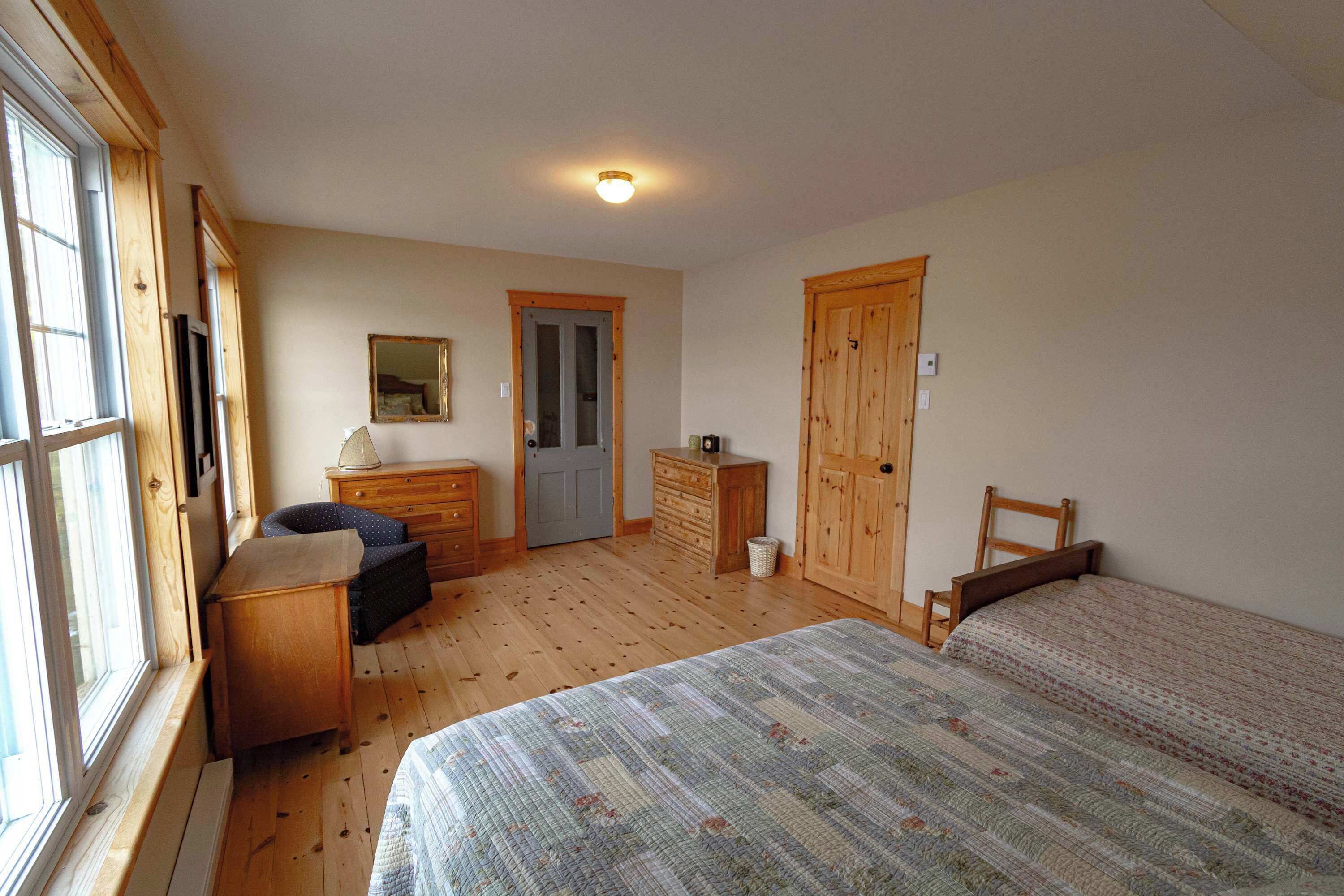 Une chambre à coucher avec un grand lit, une commode, une chaise, un bureau et une porte.