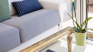 Un salón moderno con un sofá blanco, cojines a rayas, una mesa de centro de cristal con un libro y orquídeas blancas.