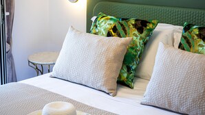 Una cama bien hecha, con un cabecero verde, dos almohadas blancas y un sombrero decorativo sobre un tapete floral.