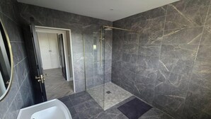 Une salle de bain moderne avec une douche à parois de verre, un lavabo blanc et des murs en marbre foncé.
