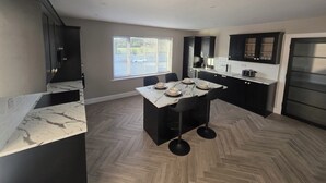Une cuisine moderne avec des meubles de couleur sombre, un plan de travail en marbre et un parquet en bois disposé en chevrons.