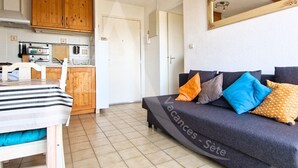 A compact living space with a kitchenette, a sofa with patterned cushions, and a dining area with a striped tablecloth.