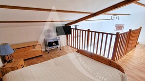 A bedroom with a large bed, wooden furniture, a TV, and a balcony with a wooden railing.