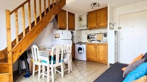A compact kitchen with wooden cabinets, a washing machine, and a dining area with chairs and a table.