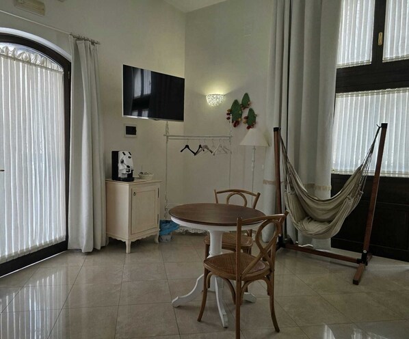 A dining area with a round table, wooden chairs, a small cabinet, a television, a wall-mounted lamp, and a hammock.