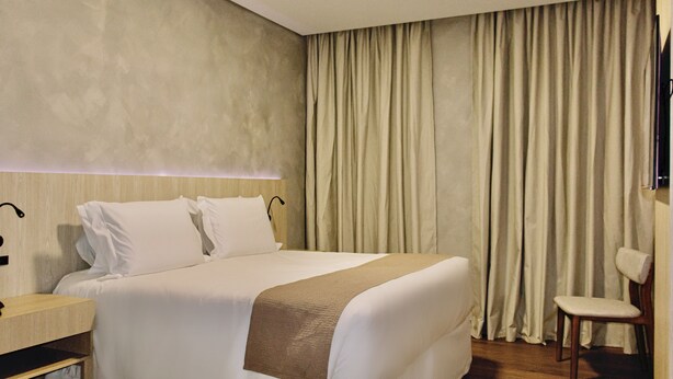 A hotel room with a bed, a wooden nightstand, a chair, and a large window with curtains. - POUSADA BIG BEAR 2 (Campos do Jordao)