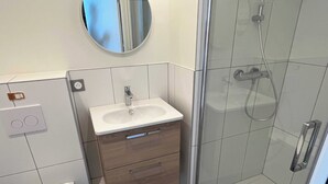 Ein modernes Badezimmer mit einer Duschkabine aus Glas, einem weißen Waschbecken mit Holzschrank und einer Toilette.