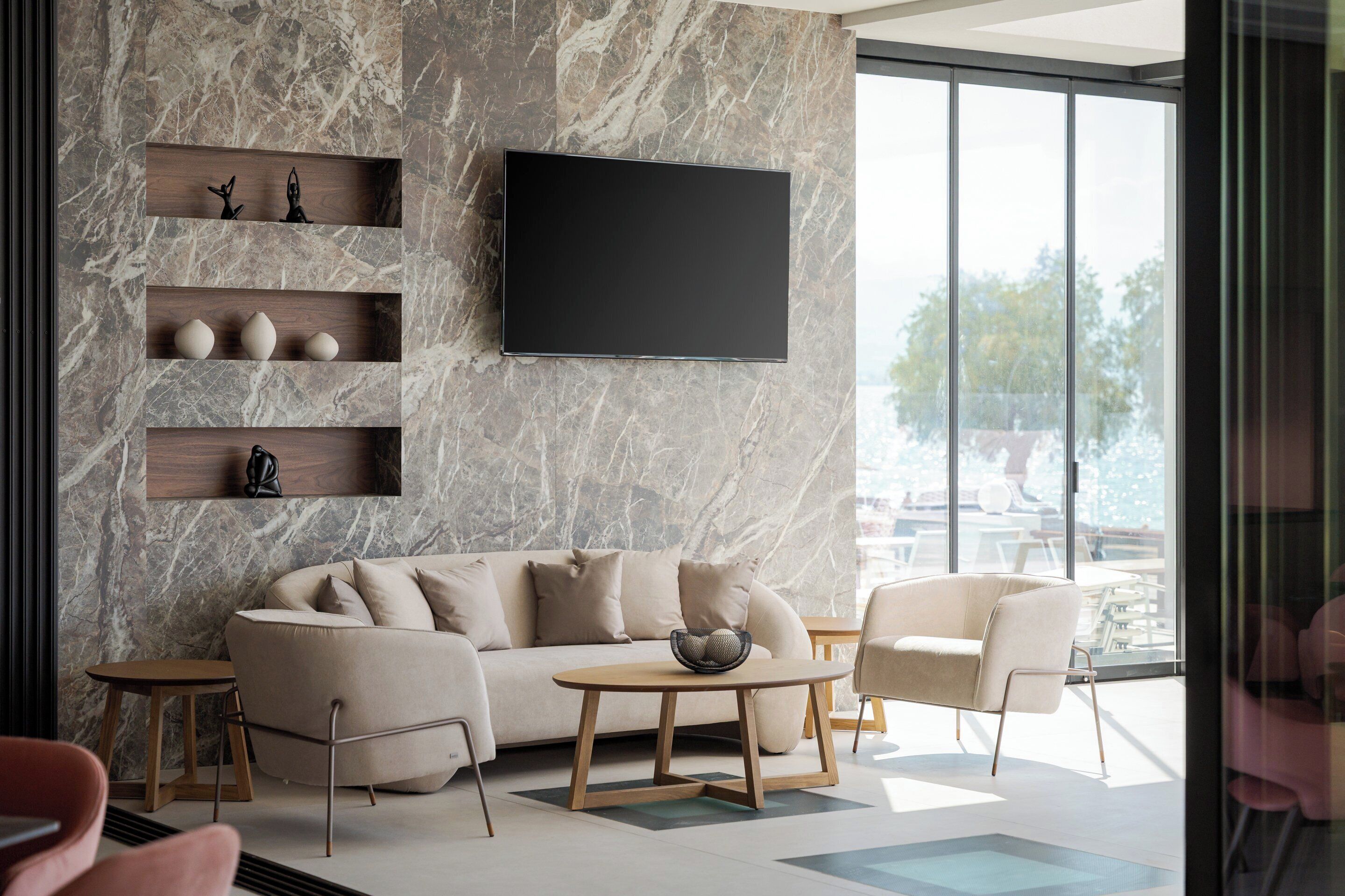 A modern living room with a marble wall, a flat-screen TV, a beige sofa, and a coffee table.