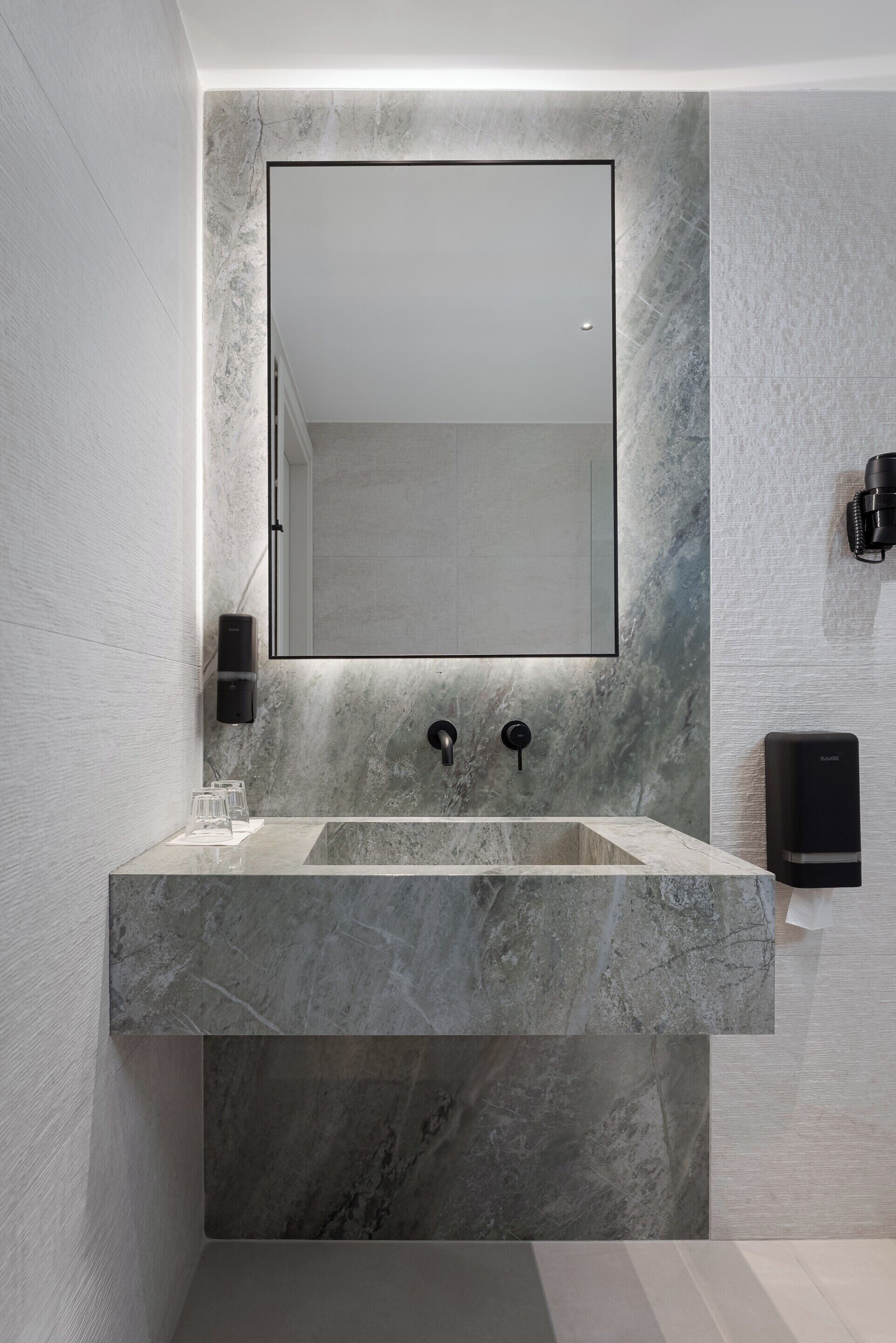 A bathroom with a large mirror, a marble sink, and a wall-mounted speaker.