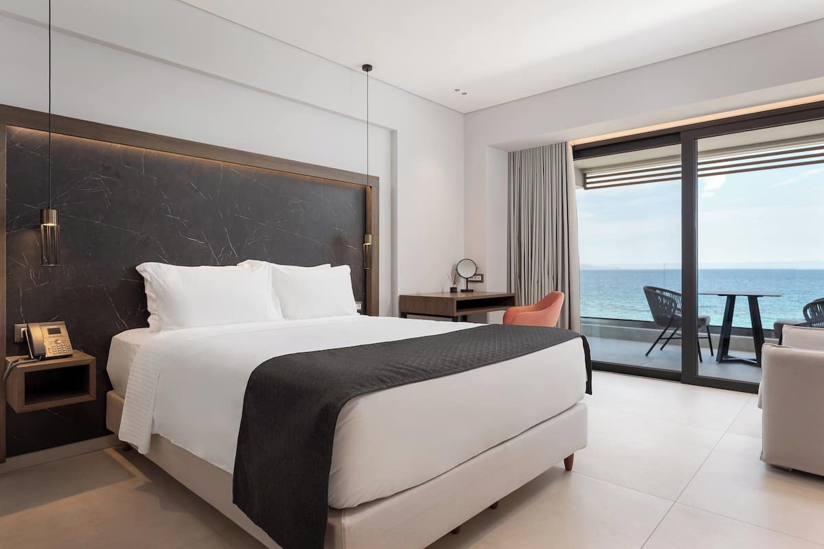 Ein modernes Hotelzimmer mit einem großen Bett, einem Schreibtisch, einem Sessel und Meerblick.