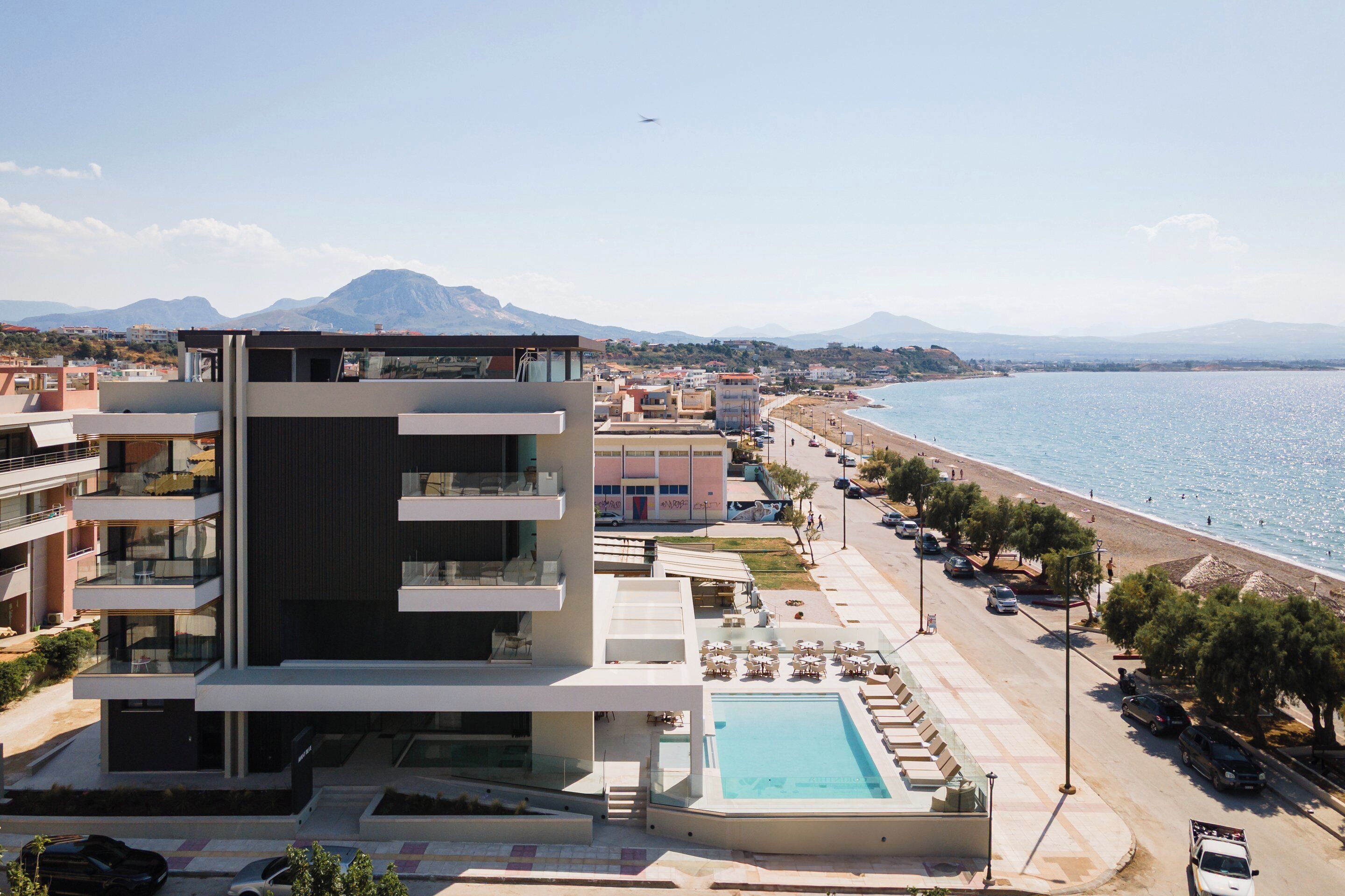 A modern hotel with a pool, beachfront view, and a mountain in the background.