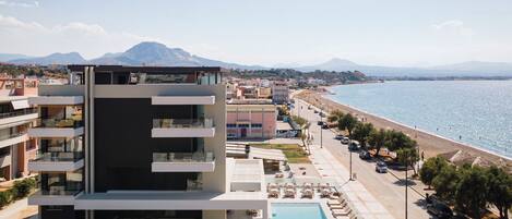 A modern hotel with a pool, beachfront view, and a mountain in the background.