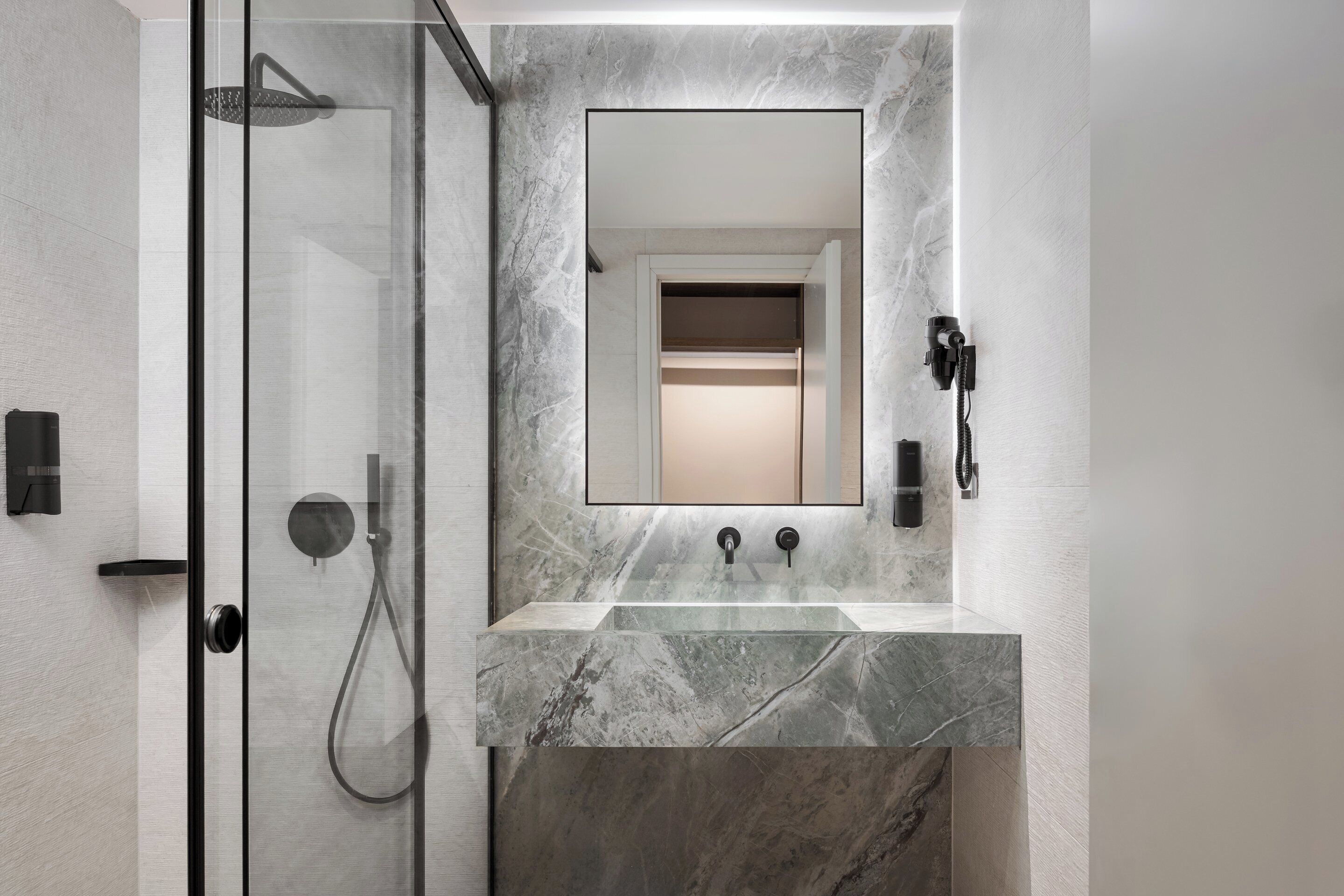 A modern bathroom with a glass-enclosed shower, a marble sink, and a large mirror.