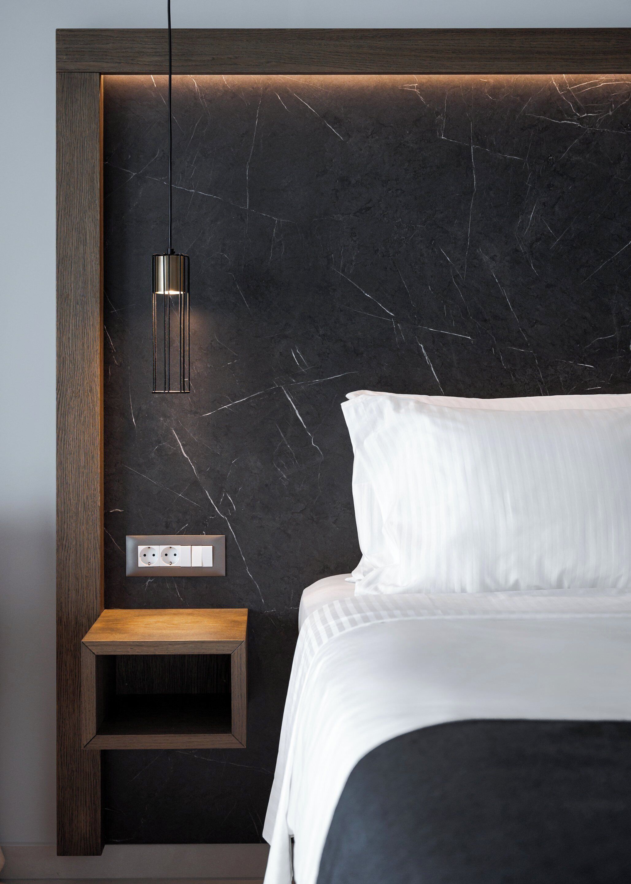 Une chambre à coucher moderne avec une tête de lit en marbre foncé, une table de chevet, une suspension et un lit parfaitement fait.