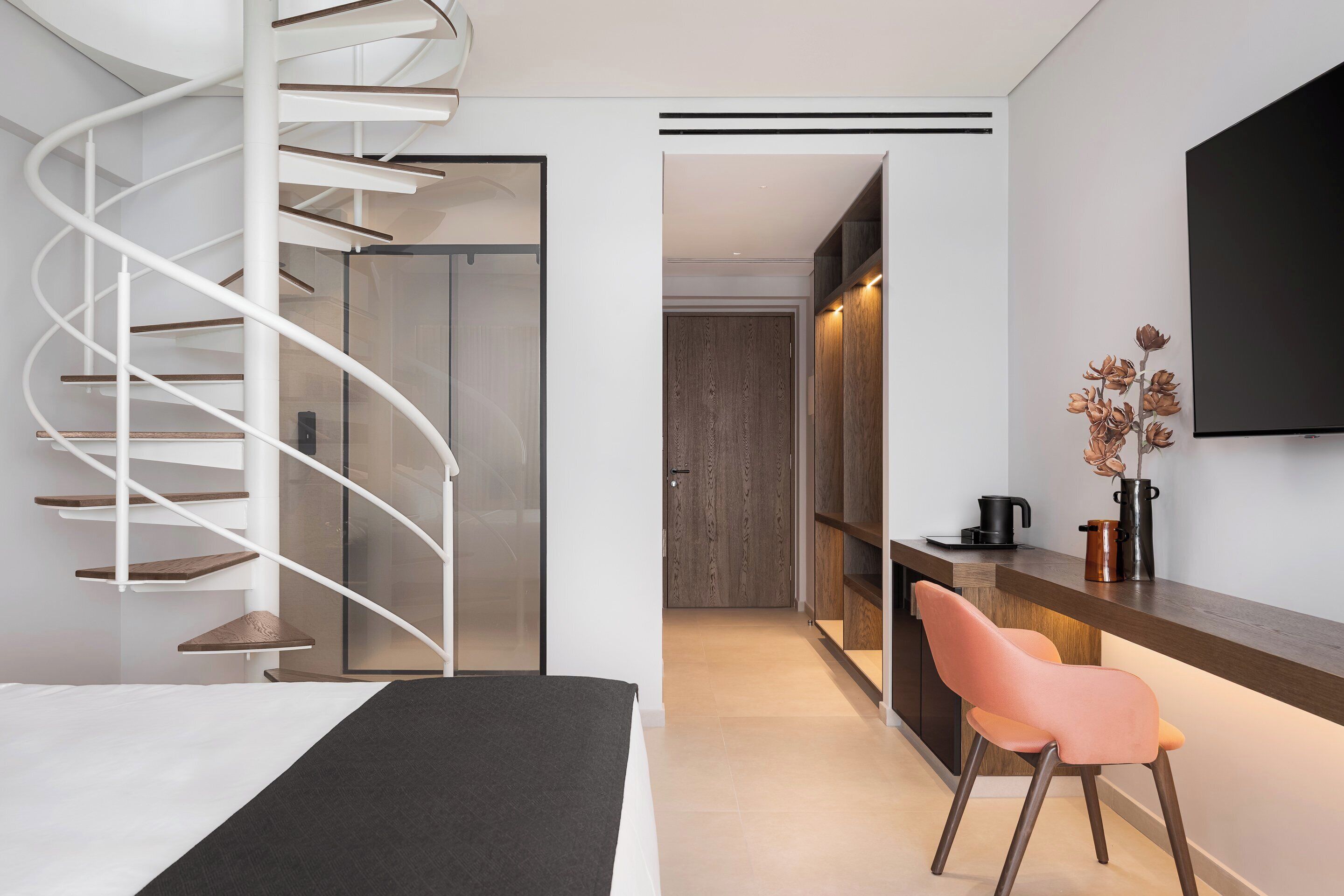 Ein modernes Hotelzimmer mit Wendeltreppe, einem Bett, einem Schreibtisch mit Stuhl und einem an der Wand befestigten Fernseher.