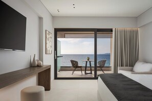 Une chambre d’hôtel moderne dotée d’un grand lit, d’une télévision, d’un balcon avec vue sur la mer et d’un coin repas avec des chaises.