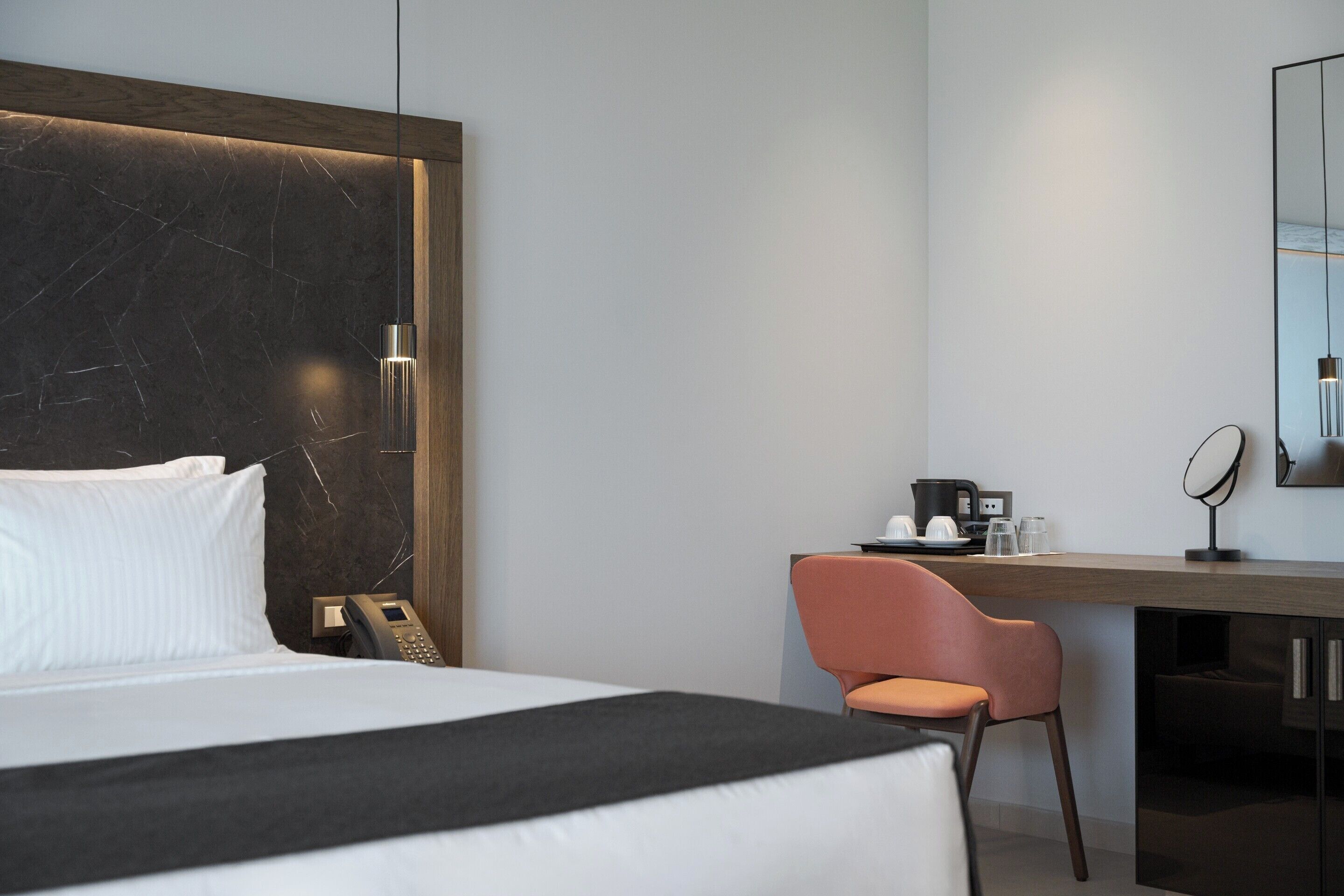 A modern hotel room with a large bed, a desk with a chair, a coffee maker, and a mirror.