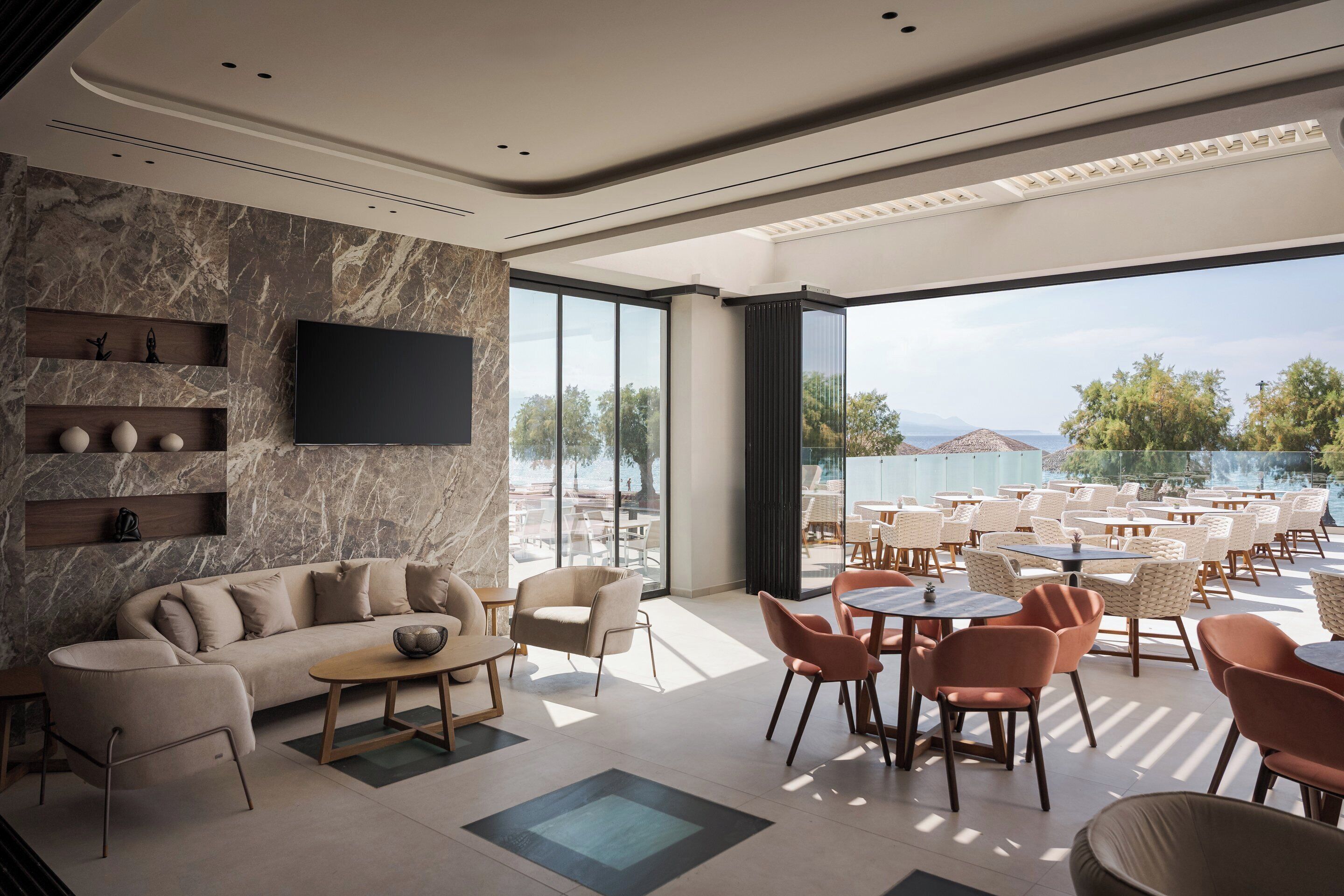 Un área de descanso moderna con sofá, sillas y mesas, amplias ventanas que ofrecen vistas al exterior.