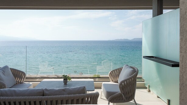 Un balcón con vista al mar, mobiliario de mimbre y un televisor de pantalla plana.