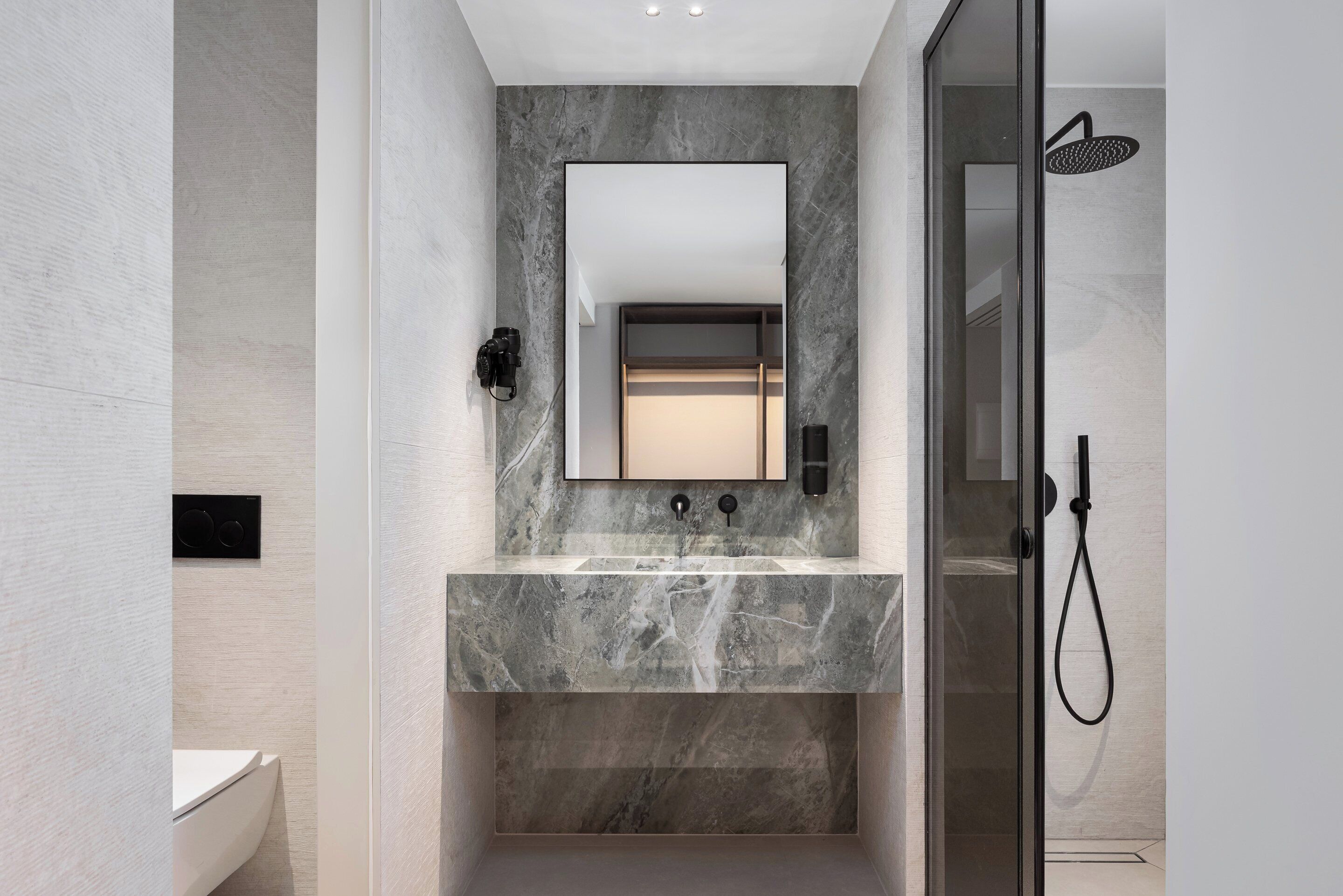 A modern bathroom with a marble sink, a large mirror, a glass-enclosed shower, and a toilet.