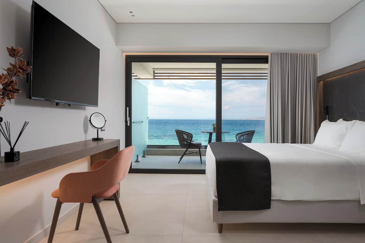Ein modernes Hotelzimmer mit Bett, Schreibtisch, Stuhl, Fernseher und einem Balkon mit Meerblick.