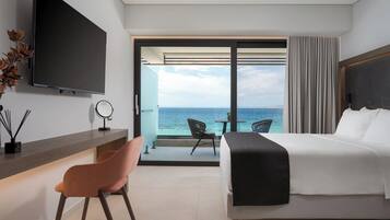 Een moderne hotelkamer met een bed, een bureau, een stoel, een televisie en een balkon met uitzicht op de oceaan.