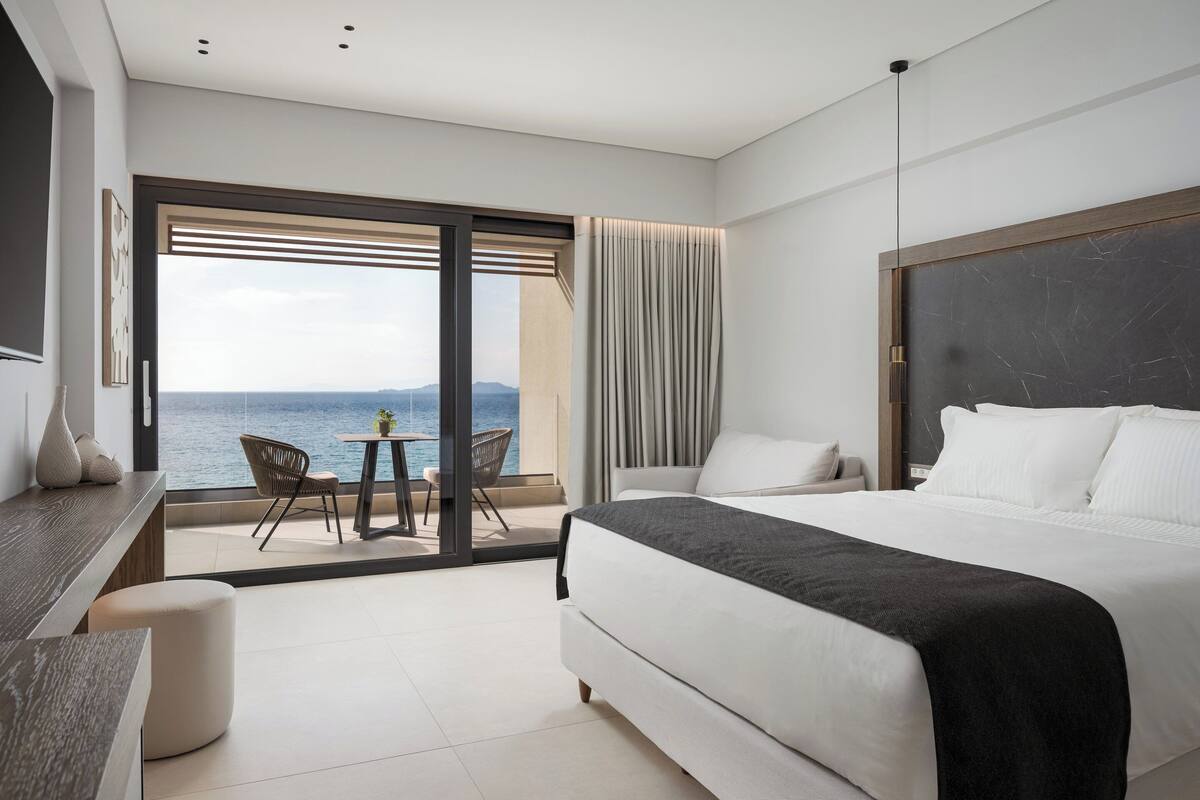 Ein modernes Hotelzimmer mit einem großen Bett, einem Schreibtisch und einem Balkon mit Meerblick.