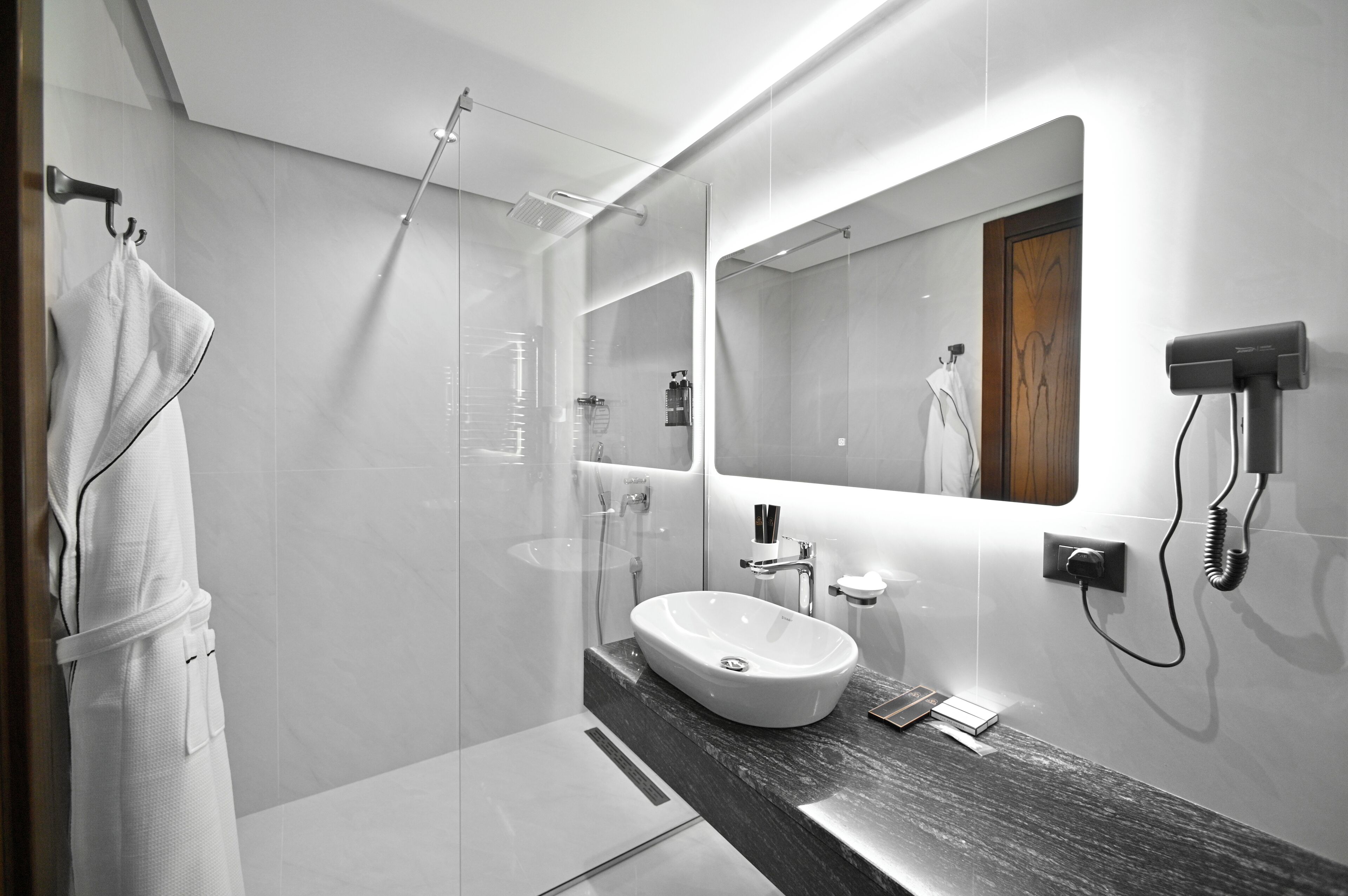 Ein modernes Badezimmer mit einer gläsernen Dusche, einem großen Spiegel und einer Marmorplatte.