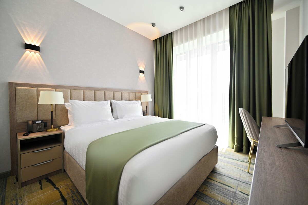 Una habitación de hotel con una cama grande, dos mesitas de noche con lámparas, un escritorio y una silla.