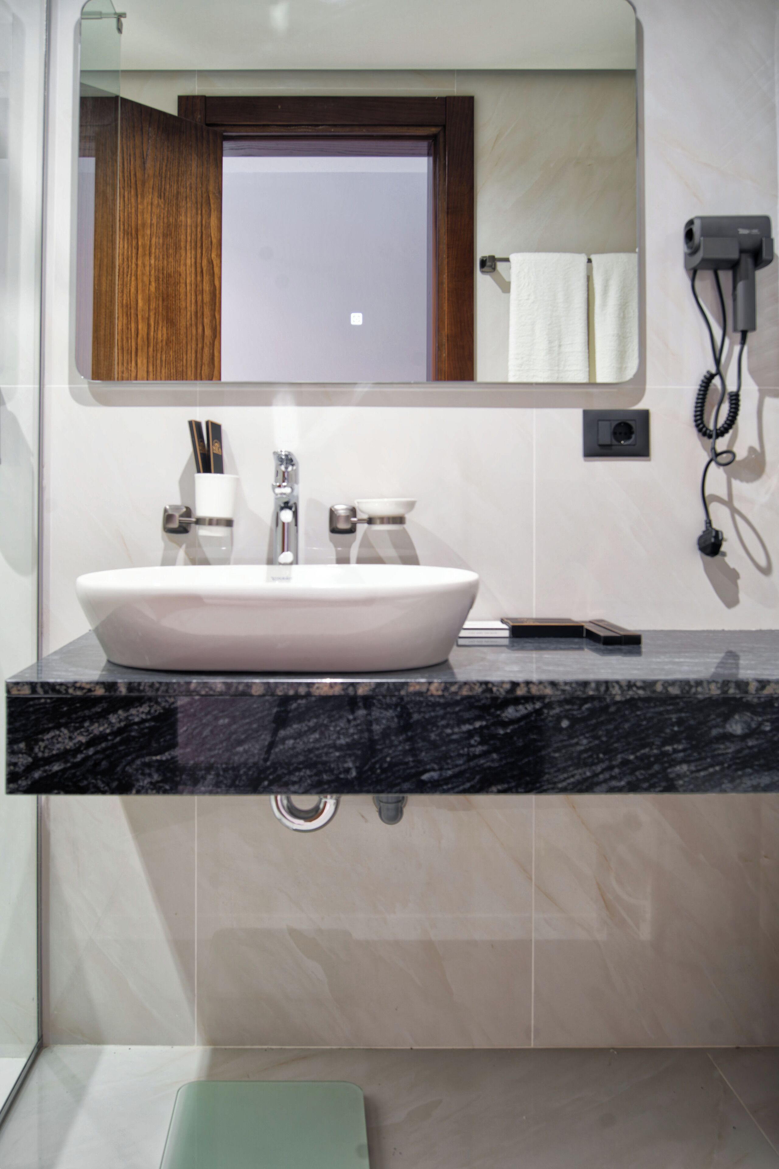 Un baño moderno con un lavamanos blanco grande, un espejo y un secador de pelo en la pared.